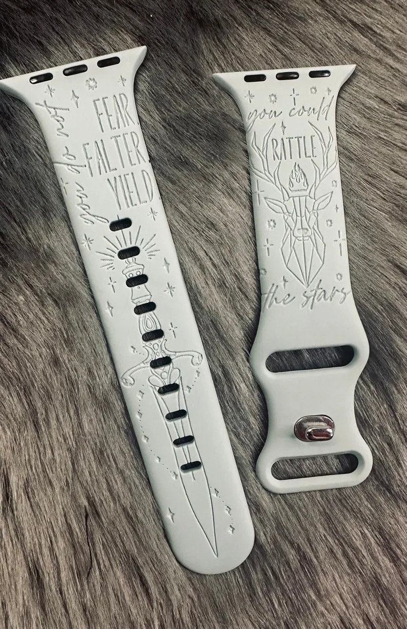 A pair of pale grey engraved Apple Watch bands with a dagger, a stag and the words you do not fear, you do not falter, you do not yield.